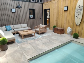 Un espacio exterior moderno con piscina, mobiliario de madera y una decoración con una tabla de surf.
