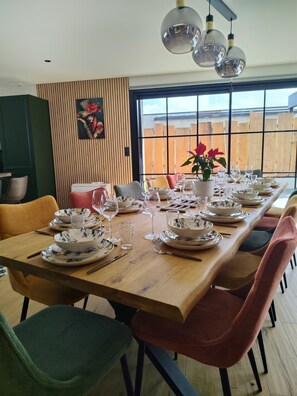 Un comedor con una larga mesa de madera dispuesta para una comida, rodeado de sillas y un ventanal con vistas.