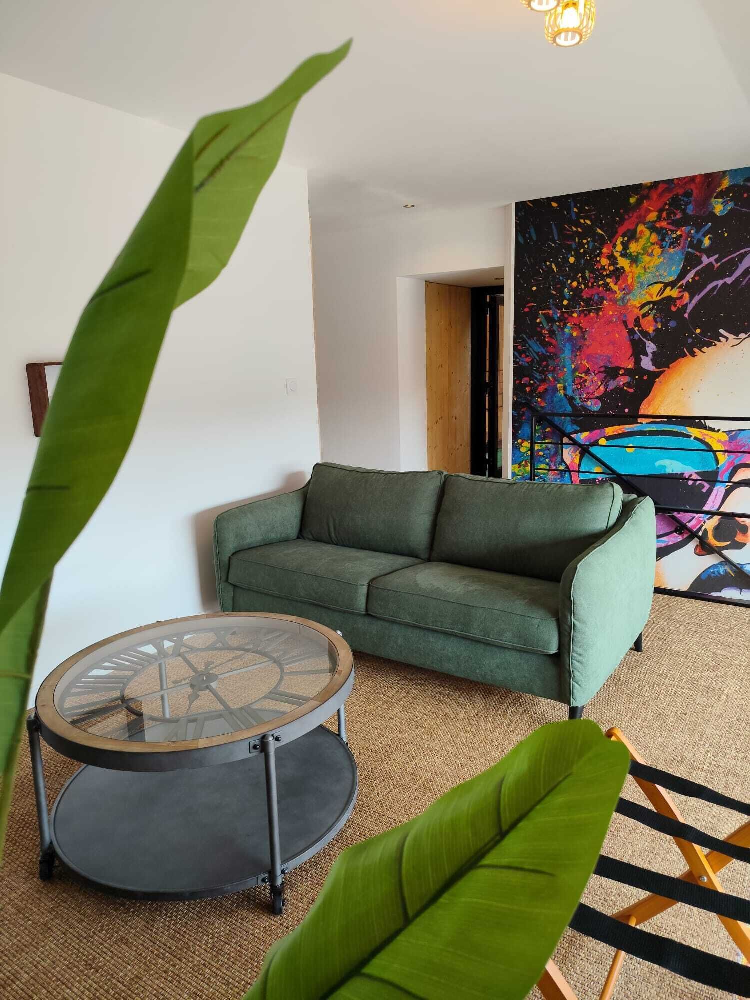 Una sala de estar con un sofá verde, una mesa de centro redonda y un cuadro abstracto grande en la pared.