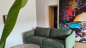 Una sala de estar con un sofá verde, una mesa de centro redonda y un cuadro abstracto grande en la pared.