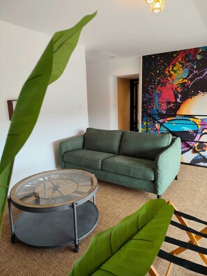 Un salon avec un canapé vert, une table basse ronde et un grand tableau abstrait accroché au mur.