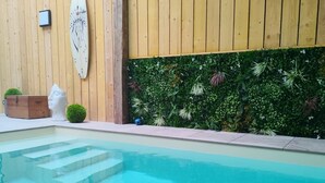 Una piscina con escalones de acceso, rodeada de paredes de madera y un muro verde con plantas.