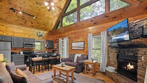 A cozy cabin interior with a dining area, living room, fireplace, and kitchen.