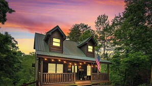 A wooden cabin with a porch, an American flag, and a 'Welcome' sign.
