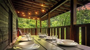 A wooden deck with a table set for dining, overlooking a forested area.