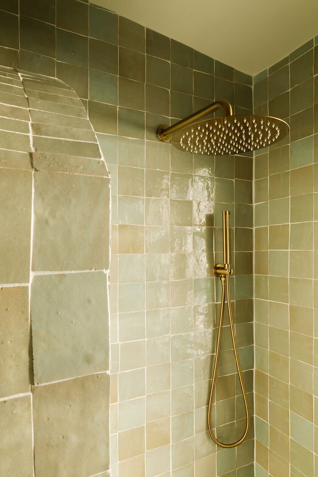 A shower with a handheld showerhead and a flexible hose, set against a tiled wall with a mix of square and rectangular tiles.