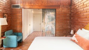 Une chambre à coucher avec un grand lit, un fauteuil bleu, un plafond en bois et une porte donnant sur une autre pièce.