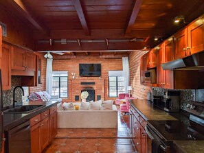 A kitchen with a brick wall, wooden cabinets, a built-in oven, and a seating area with a sofa and chairs.