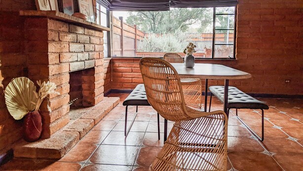 Un coin repas au style rustique, avec une cheminée en briques, des chaises en osier et un sol carrelé.