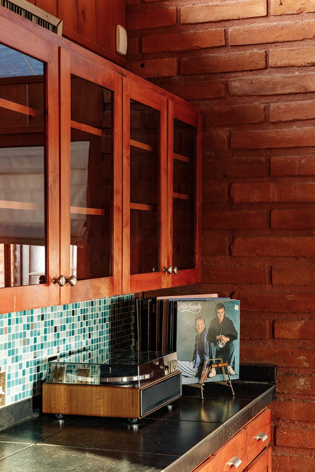 A kitchen with wooden cabinets, a tiled backsplash, and a vinyl record player.