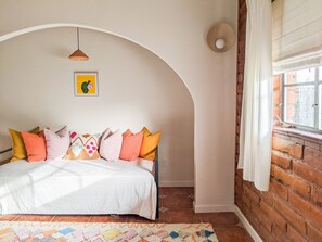 A bedroom with a white bed, colorful pillows, a hanging pendant light, and a framed picture on the wall.