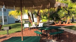 An outdoor seating area with green tables and chairs, a thatched umbrella, and palm trees. - Recently Remodeled, Very Comfy Condo Near Disney, Universal and Sea World. (Kissimmee)