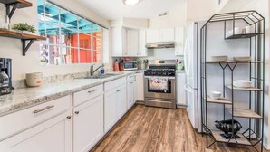 Una cocina compacta con armarios blancos, una estufa de acero inoxidable y una unidad de estanterías metálicas.