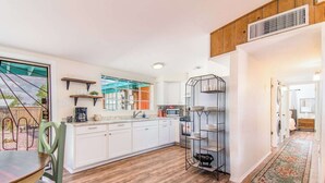 Una cocina moderna con armarios blancos, piso de madera y una unidad de estanterías de metal negro.