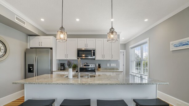 A kitchen with a large island, stainless steel appliances, pendant lighting, and a window with blinds.