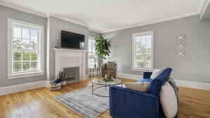 A living room with hardwood floors, a fireplace, a blue sofa, and a flat-screen TV mounted above it.