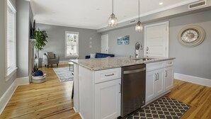 A modern kitchen with white cabinets, a stainless steel dishwasher, and pendant lighting.