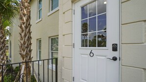 A white door with a number '6' and a security keypad, a palm tree, and a building with windows.