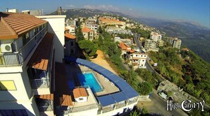A high-rise building with a rooftop swimming pool, surrounded by a hilly townscape. - Hotel Le Crillon (Broumana)