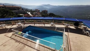 A rooftop pool with a view of distant mountains, surrounded by outdoor seating and covered areas. - Hotel Le Crillon (Broumana)