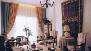 A traditional room with a chandelier, a large window with drapes, a patterned rug, and several pieces of furniture including a table and chairs. - Hotel Le Crillon (Broumana)