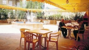 An outdoor patio with yellow canopies, a central fountain, and wooden tables and chairs. - Hotel Le Crillon (Broumana)