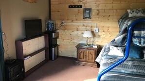 Ein Schlafzimmer mit Bett, Fernseher, Wasserspender, Lampe und einer Holzwand.