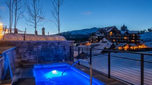 Un espace spa doté d’un jacuzzi, de murs en pierre et offrant une vue sur un chalet aux toits enneigés.