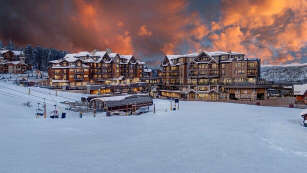Une station de ski enneigée, dotée de plusieurs bâtiments d’hébergement, d’un télésiège et offrant une vue imprenable sur les montagnes.