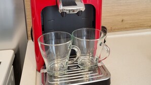 A red coffee machine with two clear glass cups on its drip tray.