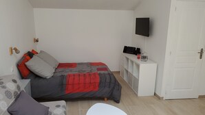 A bedroom with a bed, a bedside table with a TV, a white door, and a small white table.