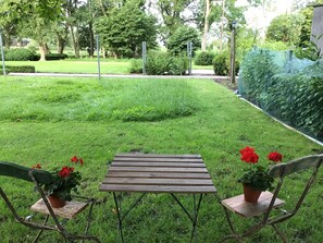 Una mesa de madera y dos sillas en un área verde al aire libre con plantas en macetas.