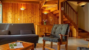 A cozy wooden interior with a sofa, armchair, and wooden staircase.