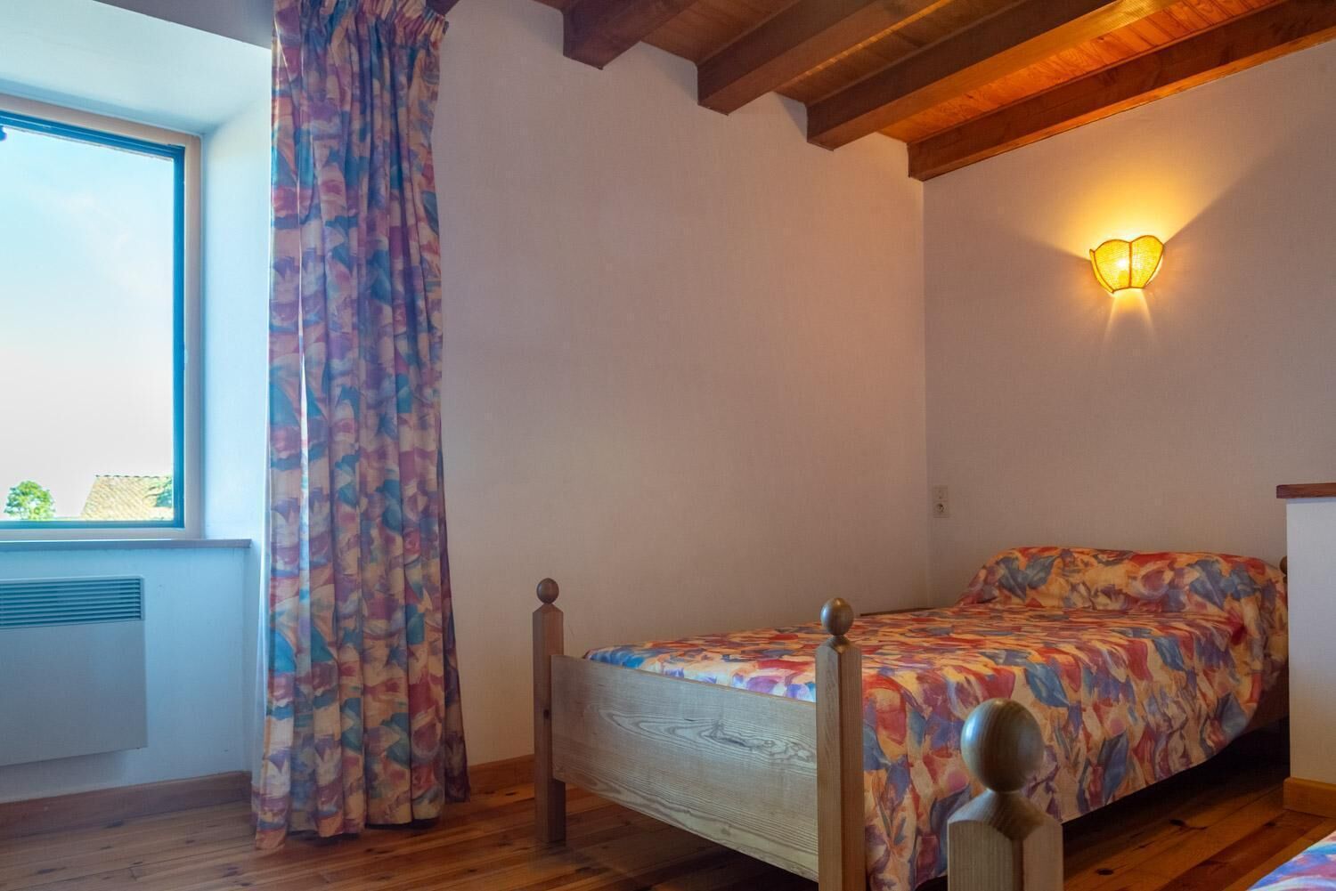 Ein Schlafzimmer mit einem Bett, einem Fenster mit Vorhängen, einer Wandleuchte und Holzbalken an der Decke.