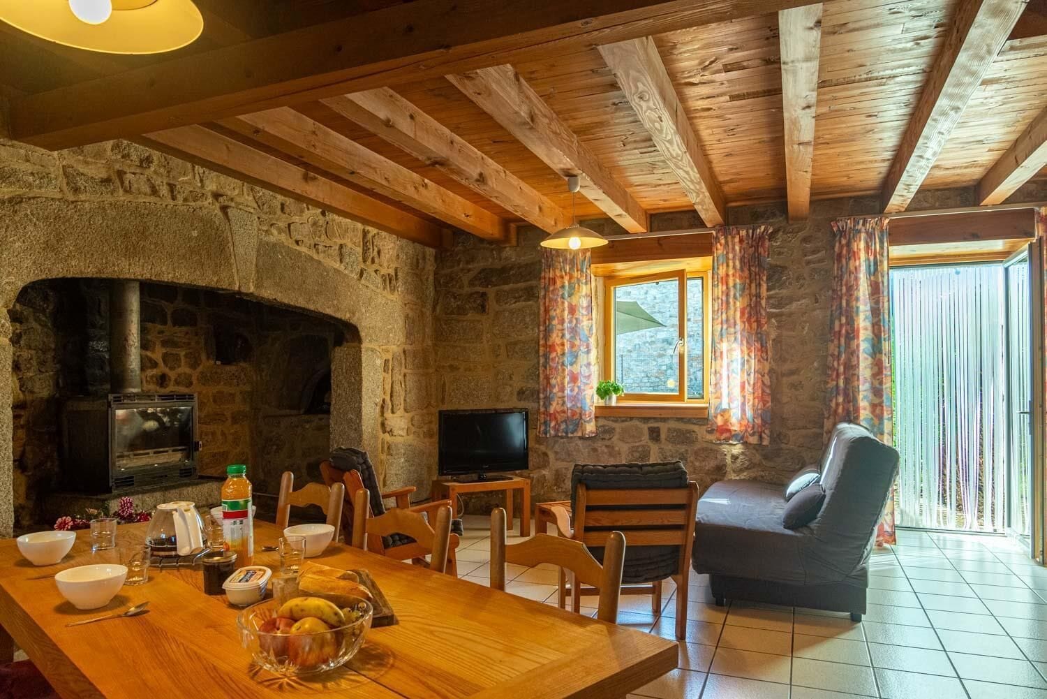 A rustic stone interior with a fireplace, wooden dining table, and a cozy seating area.