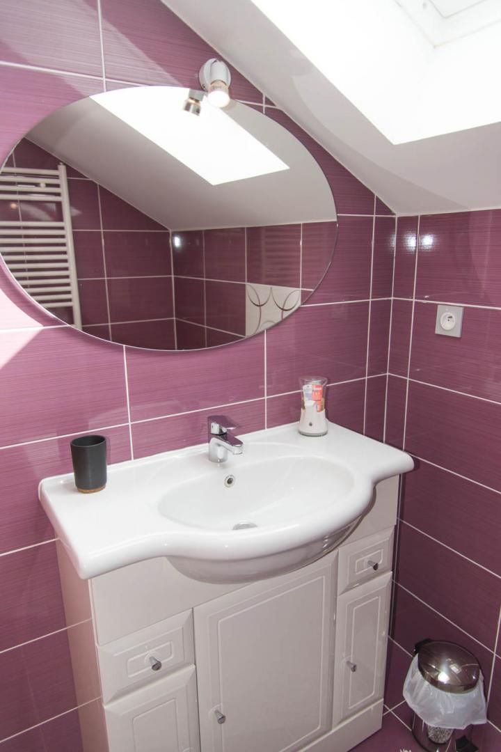 Une salle de bain avec un lavabo blanc, un miroir et des carreaux violets.