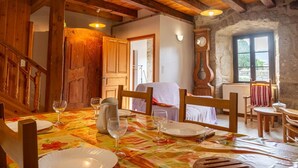 A rustic dining room with wooden beams, a table set for four, and a stone wall with a clock.