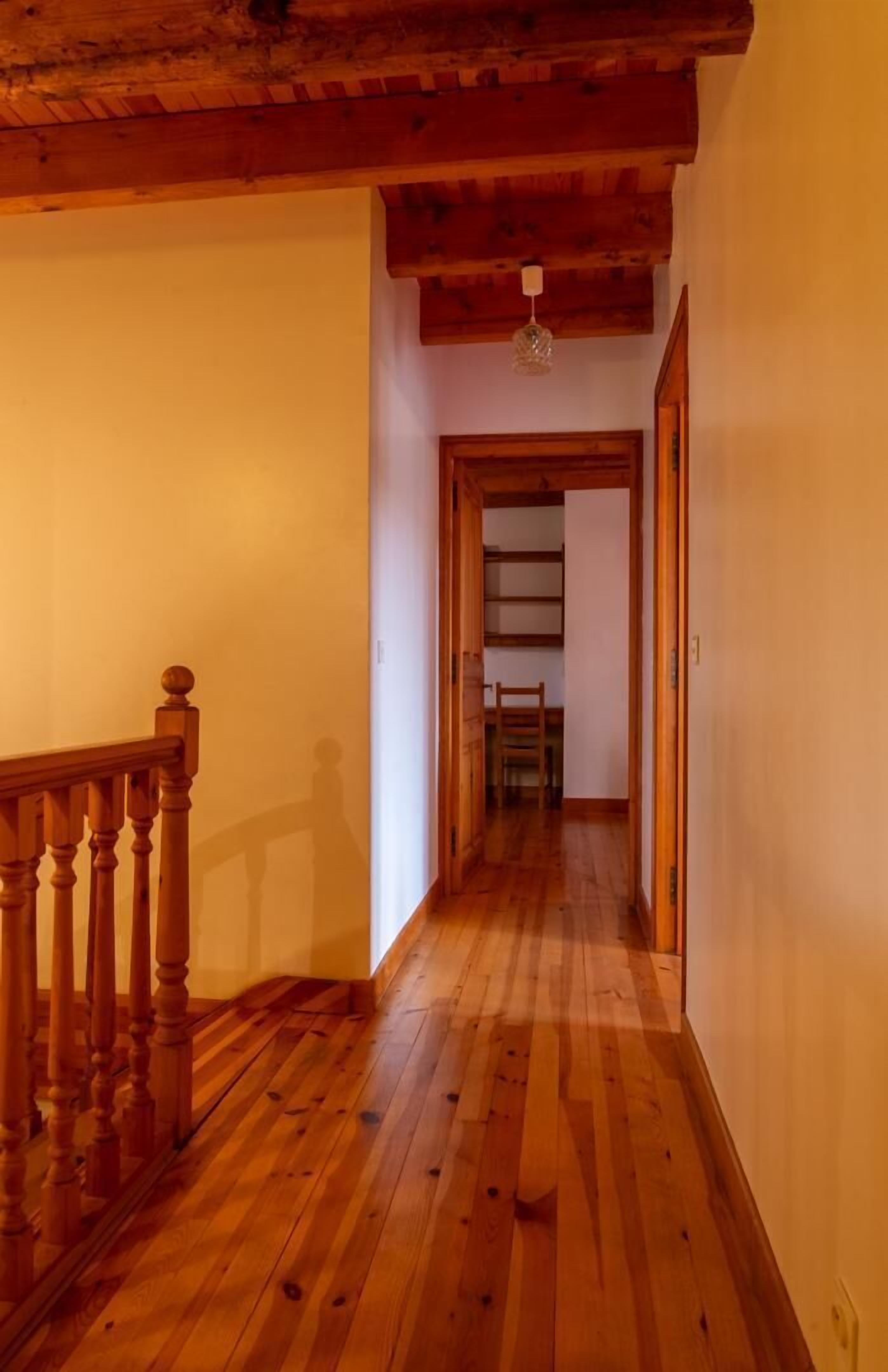Een hal met houten vloer, een houten leuning aan de linkerkant en een deur aan het einde.