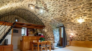 A rustic stone interior with a wooden staircase, a kitchen area, and a bed.
