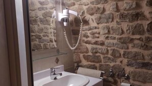 A bathroom with a stone wall, a white sink, a mirror, and a toilet.