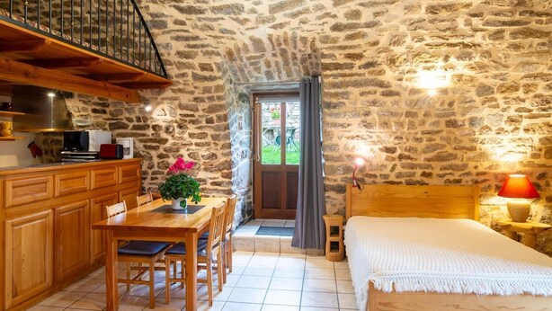 A cozy room with a stone wall, wooden furniture, a bed, and a staircase.