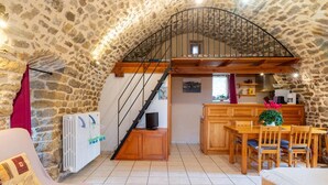 A cozy attic room with a stone ceiling, a wooden staircase, a kitchen area, and a dining space.
