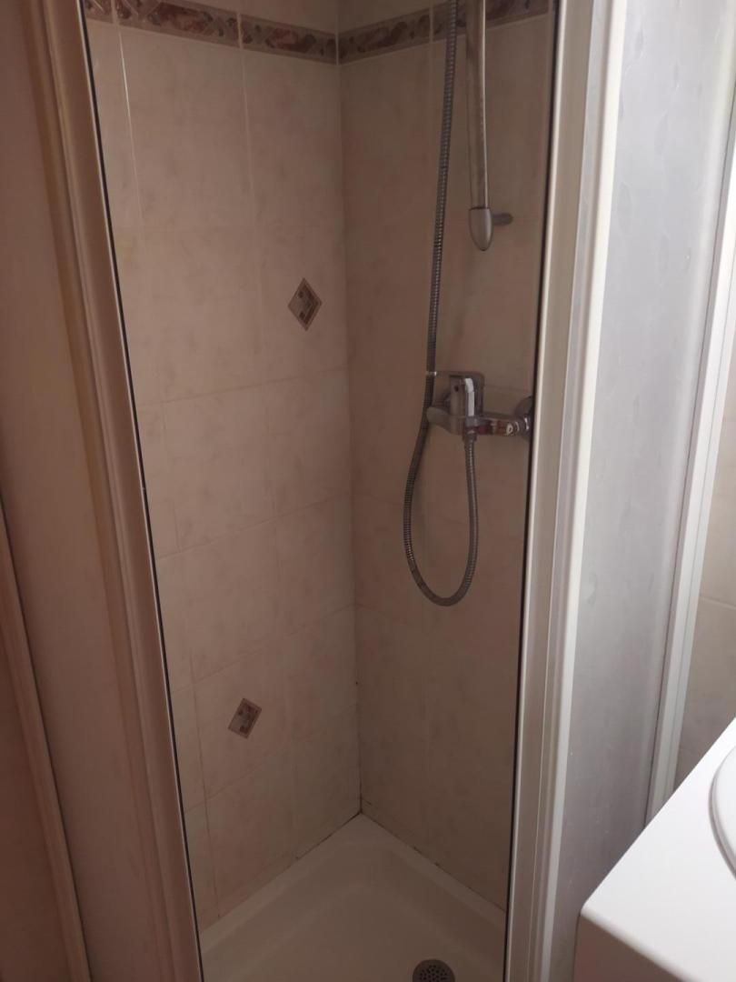 A corner shower with a handheld showerhead and a wall-mounted faucet.