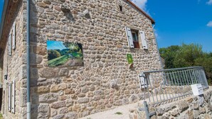 A stone building with a rustic appearance, featuring a small window with shutters, a mounted picture, and a metal railing.