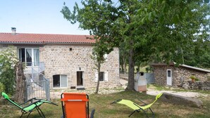 A stone house with a red-tiled roof, a stone staircase, and a small garden with two green chairs.