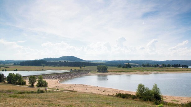 A wide river with a sandy bank and a forested hill in the background.