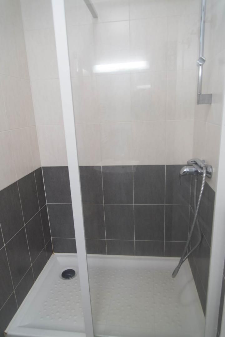 A small, enclosed shower area with a white floor and dark tiles on the walls.