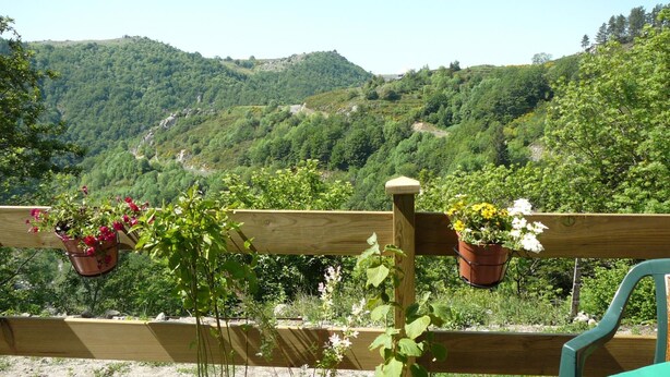 Une clôture en bois, agrémentée de plantes en pot, avec vue sur un paysage montagneux.