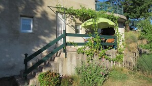 Un bâtiment doté d’un escalier menant à un balcon, entouré de verdure et d’un petit jardin.