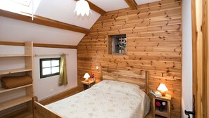 Un dormitorio acogedor con pared de listones de madera, cama con ropa de cama floral, dos lámparas de noche y un ventanal con cortinas.